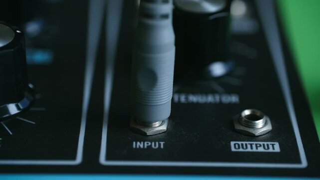 studio module synth with cables connected, man plugs grey cable into synthesizer output socket carefully, neatly arranged synthesizer connections with manual plugging in of cables in studio setting