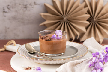 A single serving of delicious chocolate mousse in a glass, beautifully garnished with purple flowers and chocolate shavings, ready to be enjoyed.