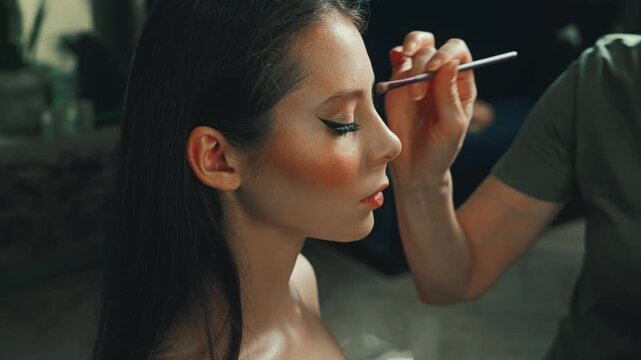 A woman with long hair in a modern beauty salon. The makeup artist enhances her eyes and natural beauty creating a stylish and polished transformation