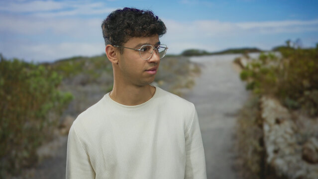 Man squints through round metal glasses wearing a white long sleeve shirt while standing on a gravel trail in forest; discomfort. - Powered by Adobe
