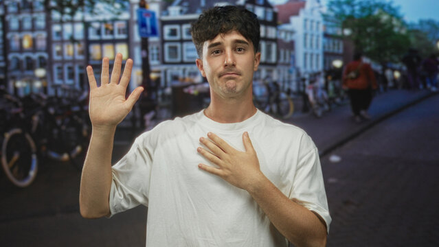 Man raises one hand and places other hand on chest on a street lined with bicycles at dusk; regret apology contrition.