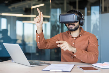 Man wearing a vr headset and headphones, smiling while pointing and interacting with virtual elements, working on future technology and innovation in a modern office