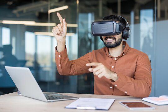 Man wearing a vr headset and headphones, smiling while pointing and interacting with virtual elements, working on future technology and innovation in a modern office