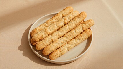 Plate of breadsticks arranged on a white dish with a beige background.