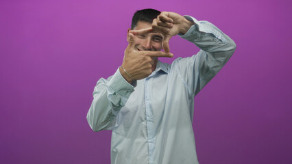 Man framing a shot with fingers and bare hands while smiling in studio with purple backdrop; creativity joy.