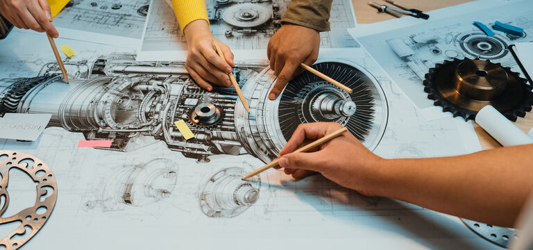 A group of professionals collaborates on a detailed engineering blueprint in a modern workspace, using pencils to highlight critical design elements and showcase teamwork. SACTR