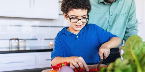 Child in blue shirt chopping vegetables in kitchen. Adult assists. Cooking together, learning, and fun in the kitchen. Bright, modern kitchen setting. Father teaching son to cook with vegetables.