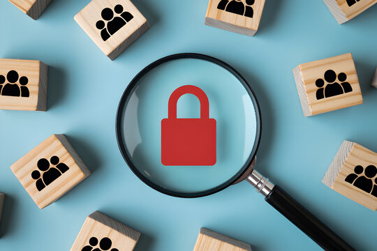 Magnifying glass focusing on a red padlock symbol surrounded by wooden blocks with group icons representing data privacy and security in a conceptual arrangement on a blue background