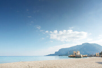 Sunny Beach With Clear Water And Mountain Backdrop Featuring A Small Pier Building