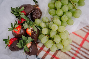Fresh strawberries dipped in chocolate alongside green grapes on a textured blanket, creating a delightful and inviting snack arrangement for gatherings or celebrations