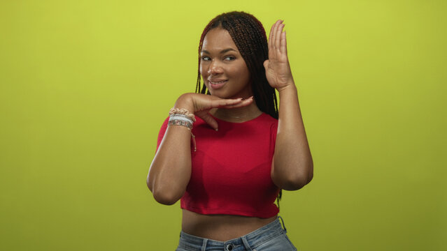 Woman in a red cropped top and jeans framing chin with raised palm in studio with lime green wall; playful confidence.