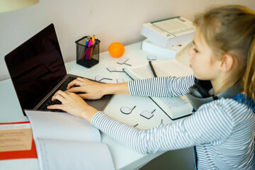 Teenage girl studying something using computer and headphones at home