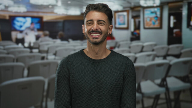 Man wearing green sweater points finger at framed painting inside building with smile; curiosity inspiration joy.