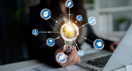 A professional woman holds a light bulb symbolizing innovation, surrounded by digital icons representing ideas and technology in a modern workspace setting. Crux