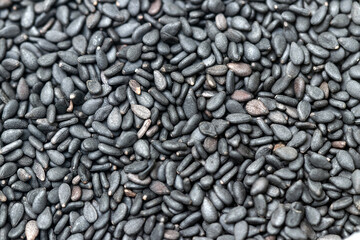 A close-up, full-frame background texture of raw, organic black sesame seeds.  showing a matte, dark gray to black color and subtle variations. Ideal for food, healthy eating, and texture concepts.