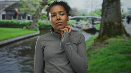 Young african american woman places hand on chin at canal edge on street; quiet introspective contemplation.