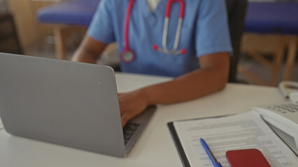Woman types on laptop in clinic building next to treatment table and medical cart; calm dedication care.