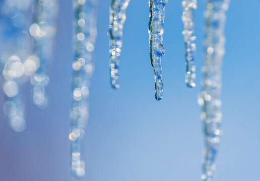 a row of shiny cold icicles dripping and melting on a sunny spring day against a blue sky - Powered by Adobe