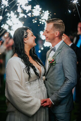 Bride and groom smiling at each other, surrounded by sparkling lights, celebrating their wedding night, capturing a moment of joy and love in an enchanting atmosphere