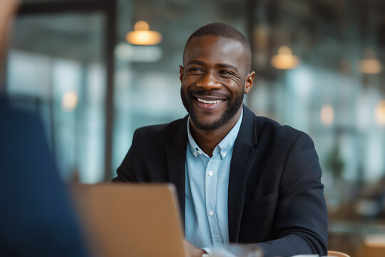 Smiling young African-American businessman, sitting at desk with laptop and talking with client, copy space