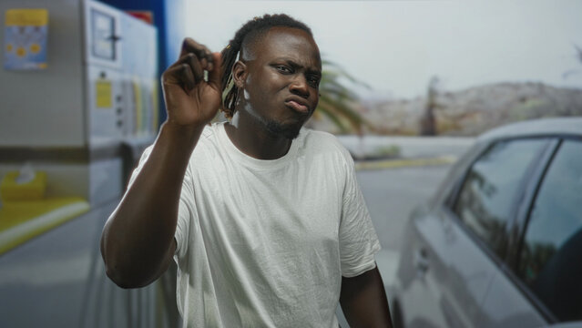 Man with hands open palms up gesturing at petrol pump on street, next to car and fuel dispenser; frustration confusion. - Powered by Adobe