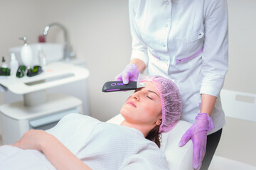 Obraz premium Hands of cosmetologist making ultrasound facial cleaning with special machine