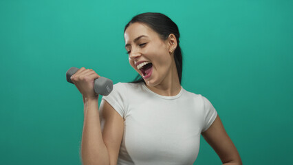 Woman smiling while exercising with dumbbell against green background showcasing fitness and energy.