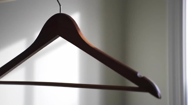 Wooden hanger on a shiny metal hook against a light gray wall with a blurred window