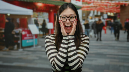 Fototapeta premium Woman with glasses on urban street smiling with joy under festive red decorations with city ambiance.