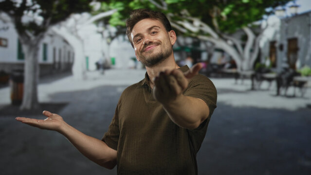 Man beckons with open hands and palm up gesture on a street plaza with trees and cafe seating; welcoming invitation.
