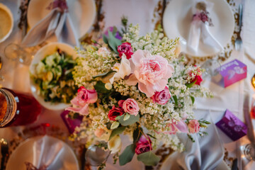 Vibrant floral centerpiece arrangement featuring pink roses, white blossoms, and greenery on elegantly set dining table, creating a romantic atmosphere for special occasions