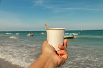white paper cup of drink in woman's palm on background of sea beach