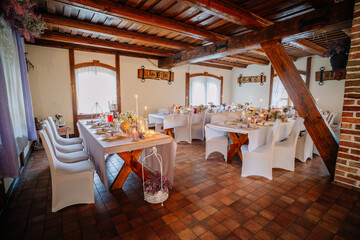 Elegant dining room with wooden beams and tables set for a festive gathering, featuring floral centerpieces and soft candlelight creating a warm atmosphere for celebrations