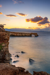 Sunset over rocky coast in Crete with tranquil sea and distant mountains