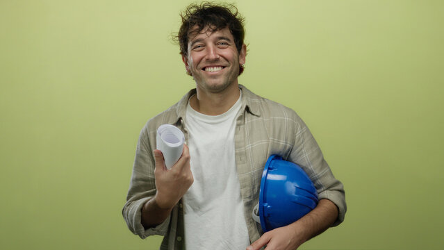 Hispanic man smiling holding blueprints and a hardhat against a green background, embodying the confident and professional demeanor of an architect or engineer.