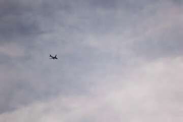 A Minimalist Shot Of A Distant Airplane Flying Against A Gray, Overcast Sky, A Concept Of A Long Journey Or Loneliness.