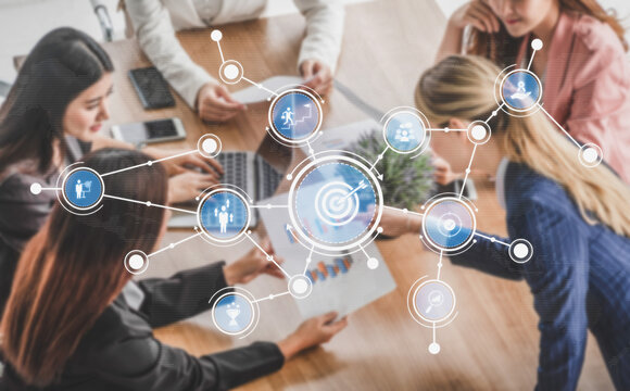 A diverse group of women collaborating in a modern office setting, using technology and focused discussions to develop strategies and achieve shared goals. Tessel