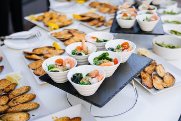 Catering buffet with edamame bowls, shrimp salads, and baked mussels outdoors