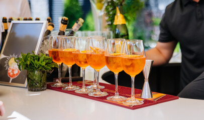 Row of Aperol Spritz cocktails with orange slices at a bar, ready to serve
