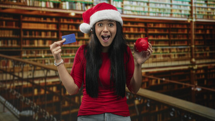 Fototapeta premium Woman holding a creditcard in one hand and a red piggybank in the other with a surprised expression in a building; holiday budgeting concern.