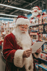 Santa Claus reading a child's Christmas wish letter in shopping mall toy section with shelves of toys behind him