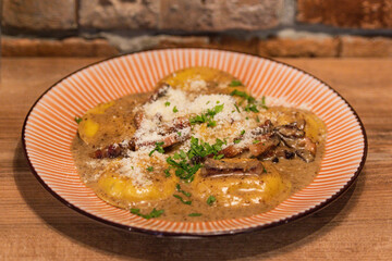 Homemade ravioli with porcini mushrooms and crispy guanciale, served in a creamy sauce and garnished with parsley and parmesan cheese 
