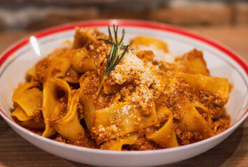 Delicious plate of pappardelle Bolognese topped with rich meat sauce and garnished with rosemary and grated Parmesan cheese