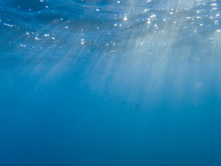 Dark blue ocean surface seen from underwater. Abstract waves underwater and rays of sunlight shining through, Sun light rays undersea deep, Underwater background with sea bottom, Mediterranean sea.