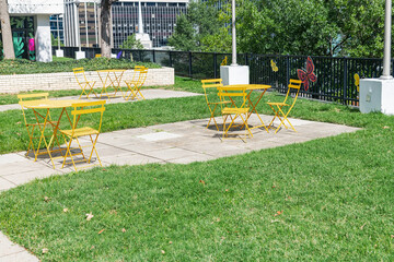 Bright yellow picnic tables in urban setting under midday sun. Modern public seating area with clean concrete background.