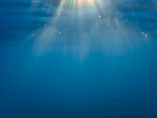 Dark blue ocean surface seen from underwater. Abstract waves underwater and rays of sunlight shining through, Sun light rays undersea deep, Underwater background with sea bottom, Mediterranean sea.