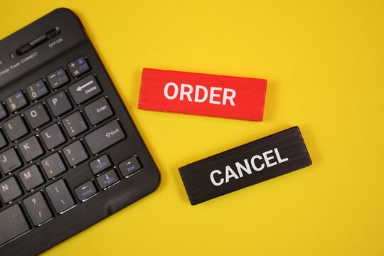 A close-up showing a laptop keyboard next to two red and black wooden blocks labeled ORDER and CANCEL. An yellow background. Suitable for business and e-commerce.