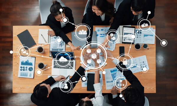 A high-angle view of a diverse team engaged in a collaborative business meeting, surrounded by data charts and technology, reflecting innovation and teamwork in a modern workspace. Amity