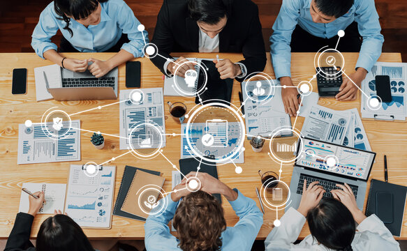 A diverse group of professionals engages in a collaborative business meeting with laptops and documents, analyzing graphs and data to strategize and innovate effectively. Amity - Powered by Adobe