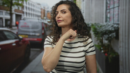 Woman holds hand at her neck in a cut throat gesture on a busy urban street outdoors amid parked cars and buildings; threat.